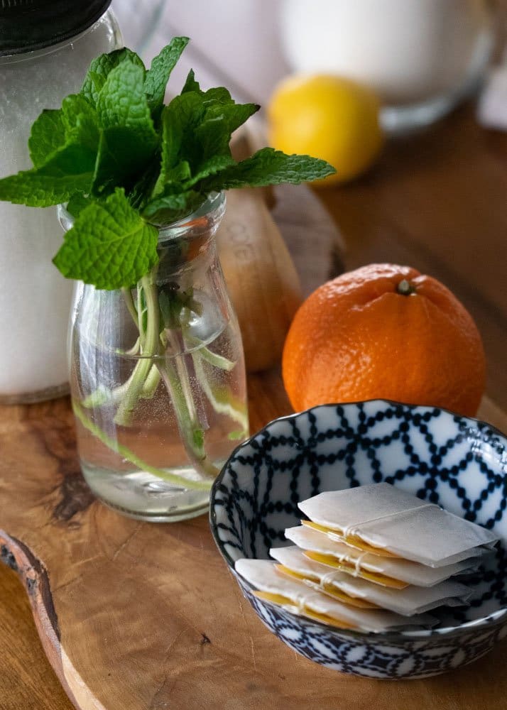 mint, tea bags, orange, lemon, and sugar on table