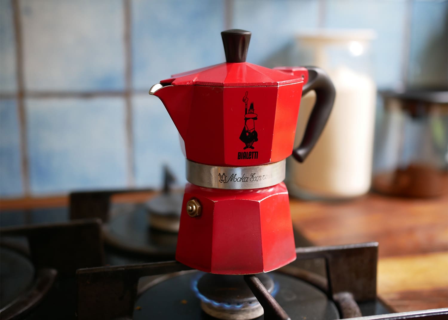 a red 6 cup moka pot sitting on gas stove