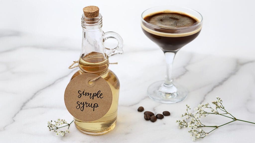 A Bottle Of Simple Syrup Next To A Shakerato In A Martini Glass