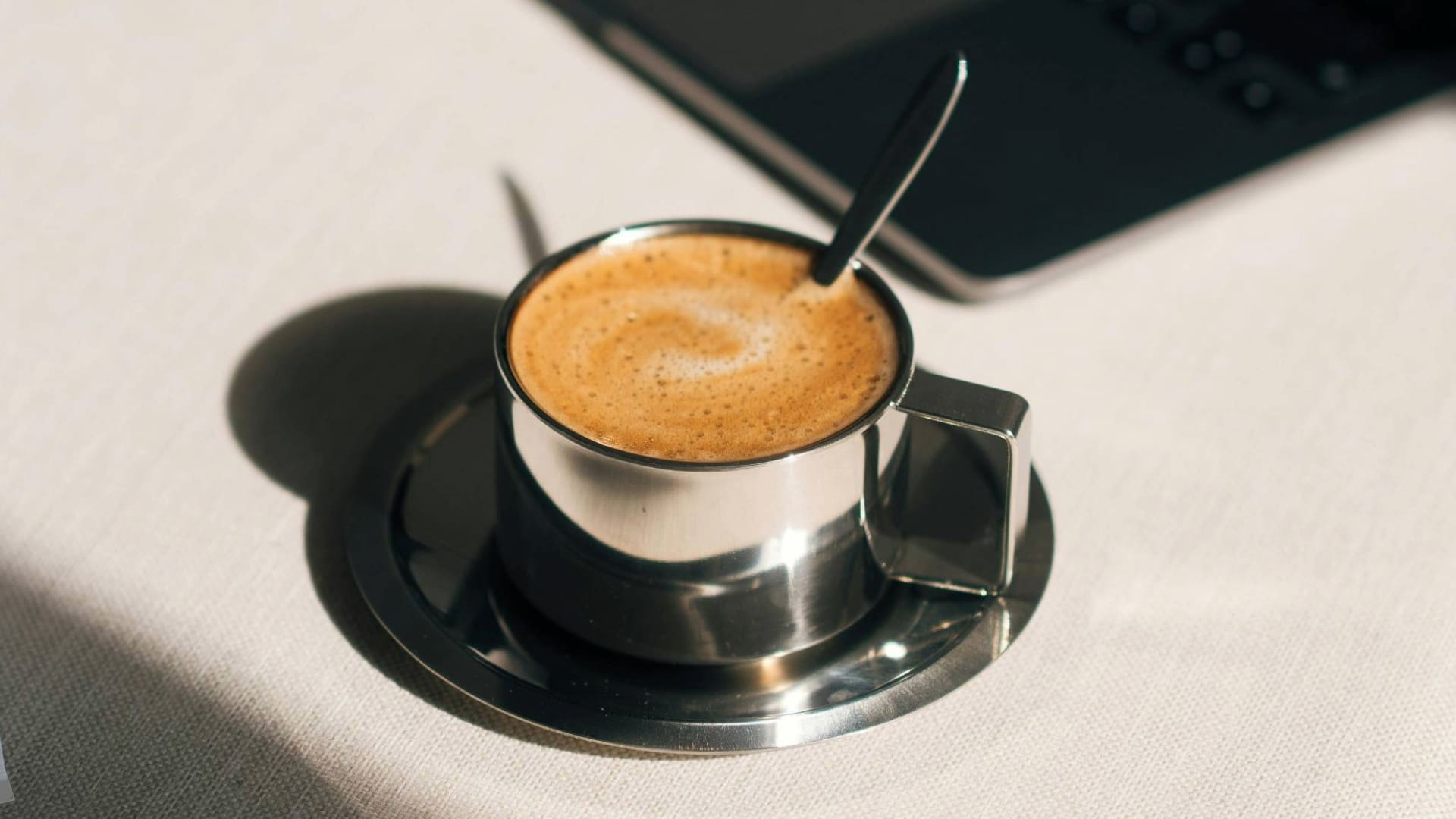 Espumita on top of espresso in a metal espresso cup with metal spoon