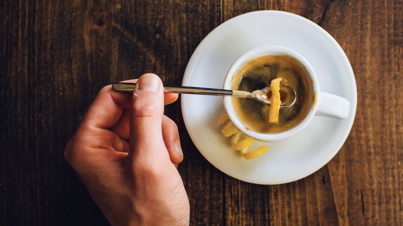 taking lemon rind out of a cup of espresso using a long teaspoon