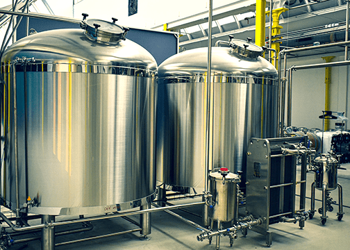 Industrial coffee fermentation setup with two large stainless steel tanks and a connected processing unit. 