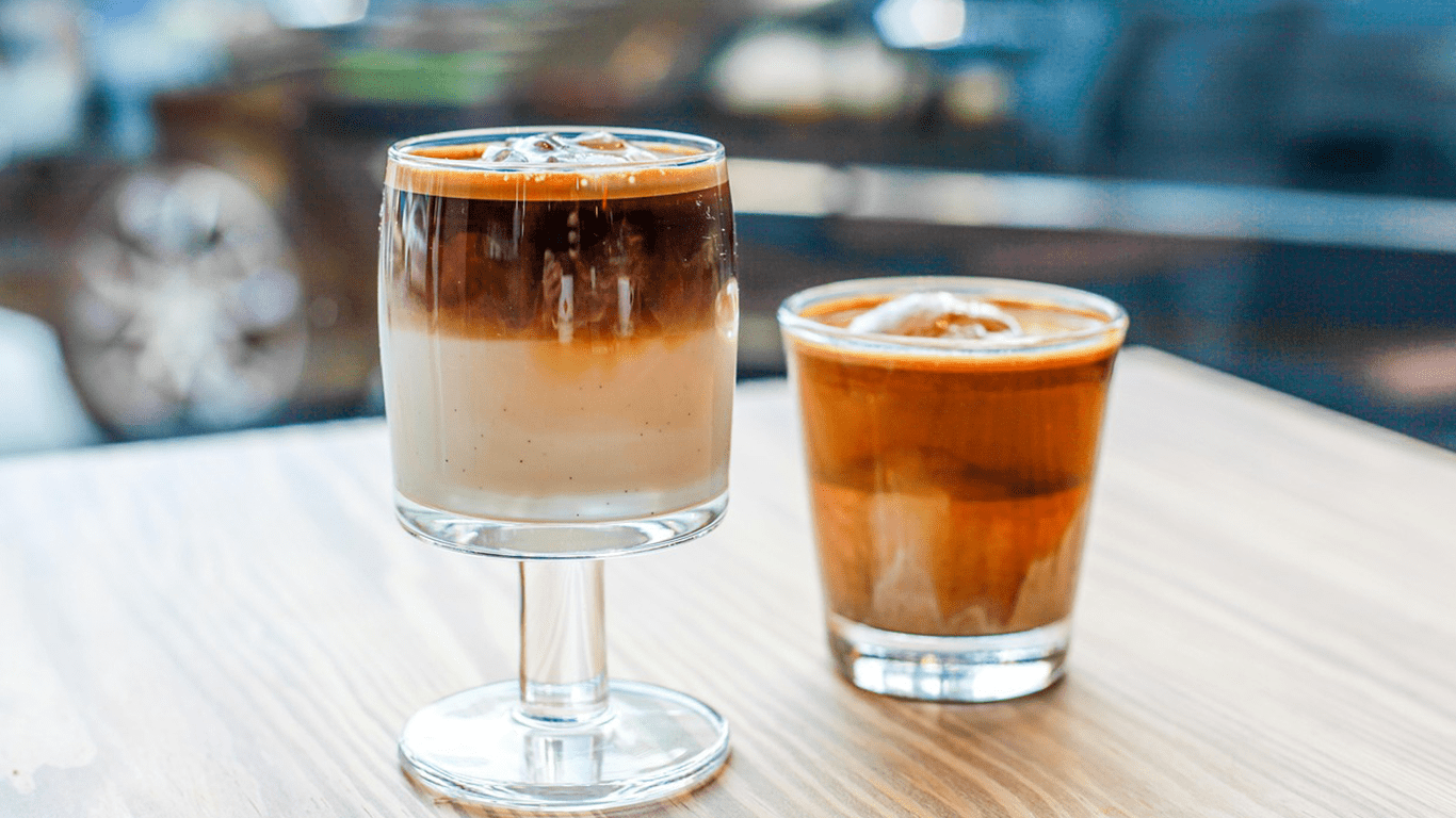 Image of two iced Cuban coffee drinks on a wooden table—one layered, one blended, both served with ice.