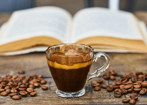 Glass Cup Of Espresso With A Rich Crema Sits On A Wooden Surface, Surrounded By Roasted Coffee Beans.