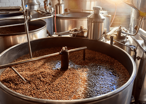 Advanced Coffee Fermentation Techniques Most Roasters Still Don't Know About Large stainless steel fermentation tank filled with grains and liquid, equipped with mechanical stirring arms and fluid transfer piping.