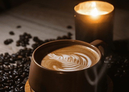 Advanced Coffee Fermentation Techniques Most Roasters Still Don't Know About Close-up of a steaming cup of coffee with leaf-shaped latte art, served in a brown ceramic cup on a wooden surface.