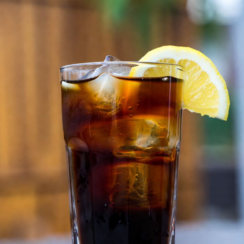 A tall glass of Mazagran lemon espresso served over ice with a lemon wheel garnish
