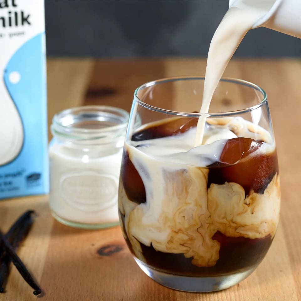 Oat milk sweet cream being poured over ice in a glass before adding cold brew coffee